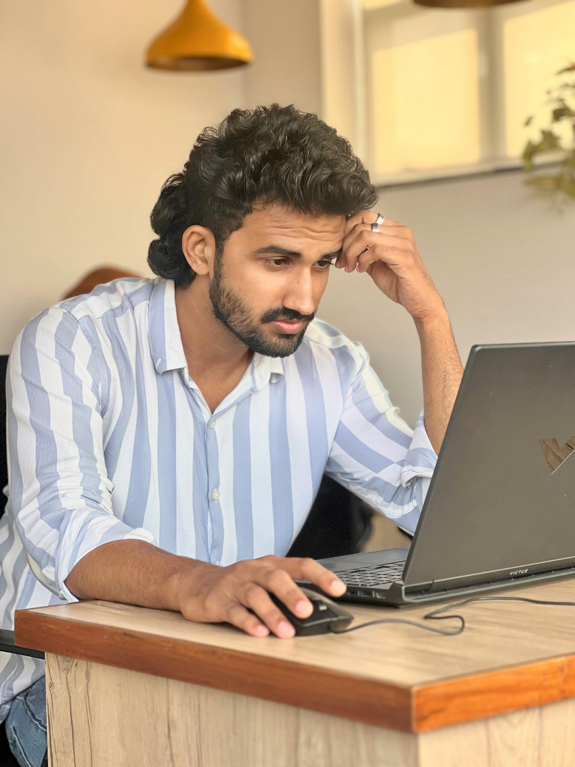 Young man in striped shirt focused on work using a laptop in a modern office setting.